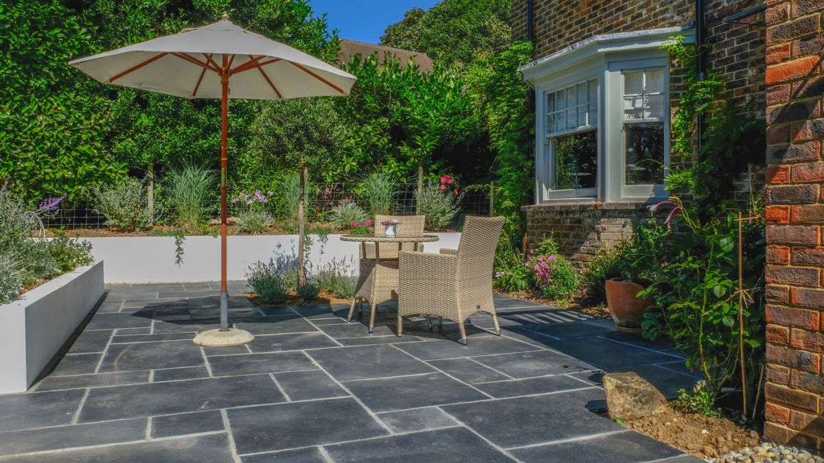 Grey Indian sandstone patio installed with a parasole and garden furniture